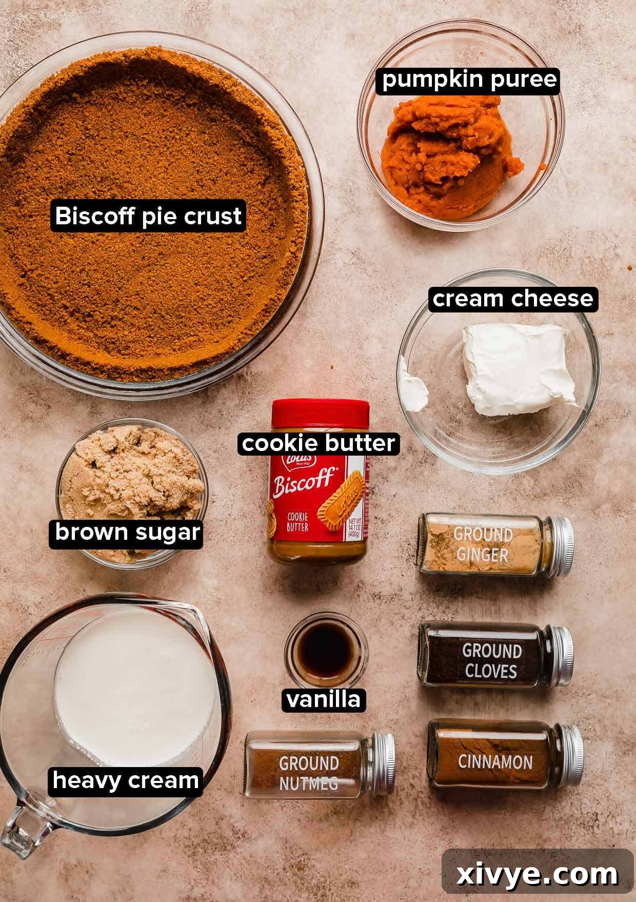 Various ingredients for Biscoff Pumpkin Pie, including Biscoff cookies, pumpkin puree, spices, and cream cheese, neatly arranged on a beige background.