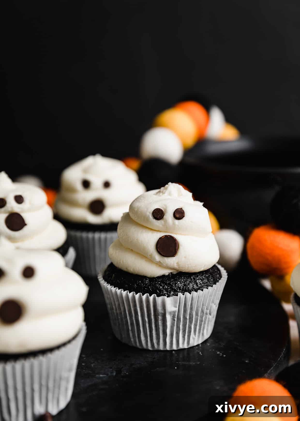 Ghost Cupcakes against a black background. Each cupcake has a unique facial expression made with chocolate chips.