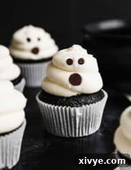 Ghost Cupcakes against a black background. The white frosting ghosts have chocolate chip eyes and mouths, creating a spooky yet adorable effect.