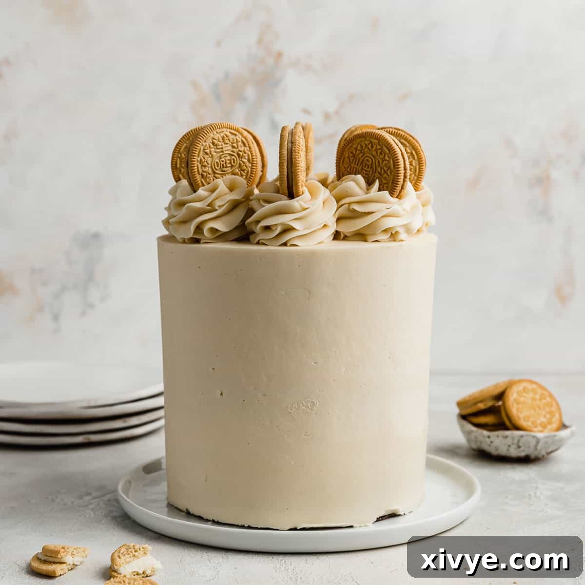 A stunning three-layer Golden Oreo Cake, elegantly presented on a white plate against a white textured background, highlighting its golden hues and creamy frosting.