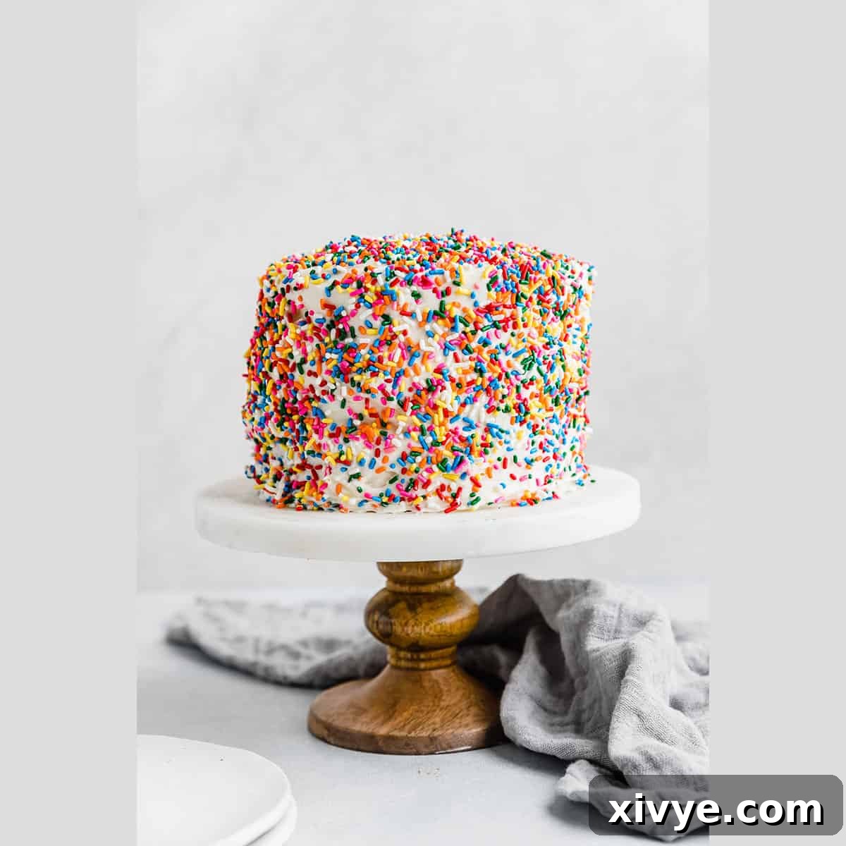 A festive, sprinkle-covered Smash Cake Recipe proudly displayed on a white marbled cake stand, ready for a celebration.