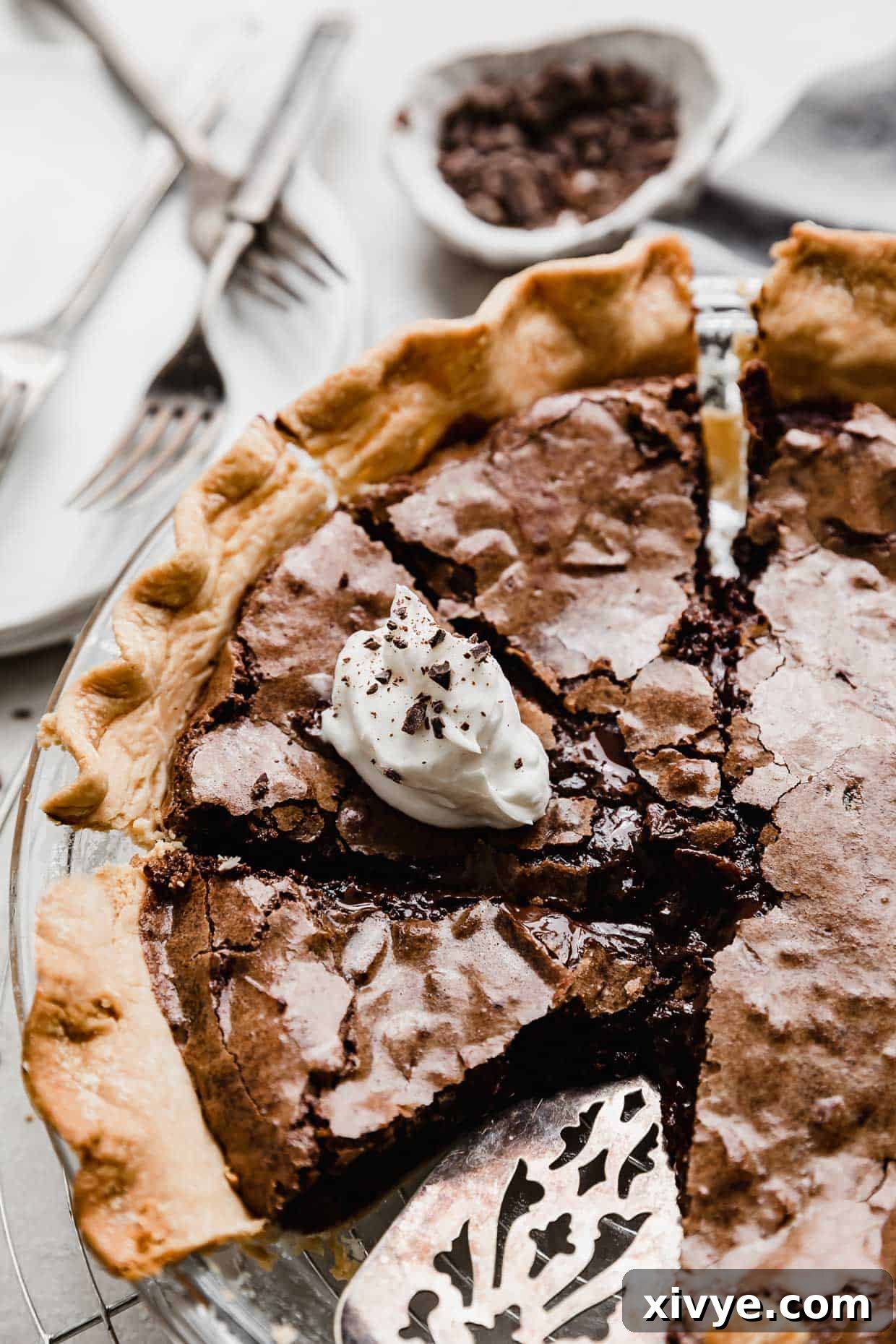 A Brownie Pie cut into slices, with one slice topped with white whipped cream and chocolate shavings.