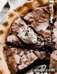 A brownie pie sliced into several servings, with one slice topped with white whipped cream and chocolate shavings.