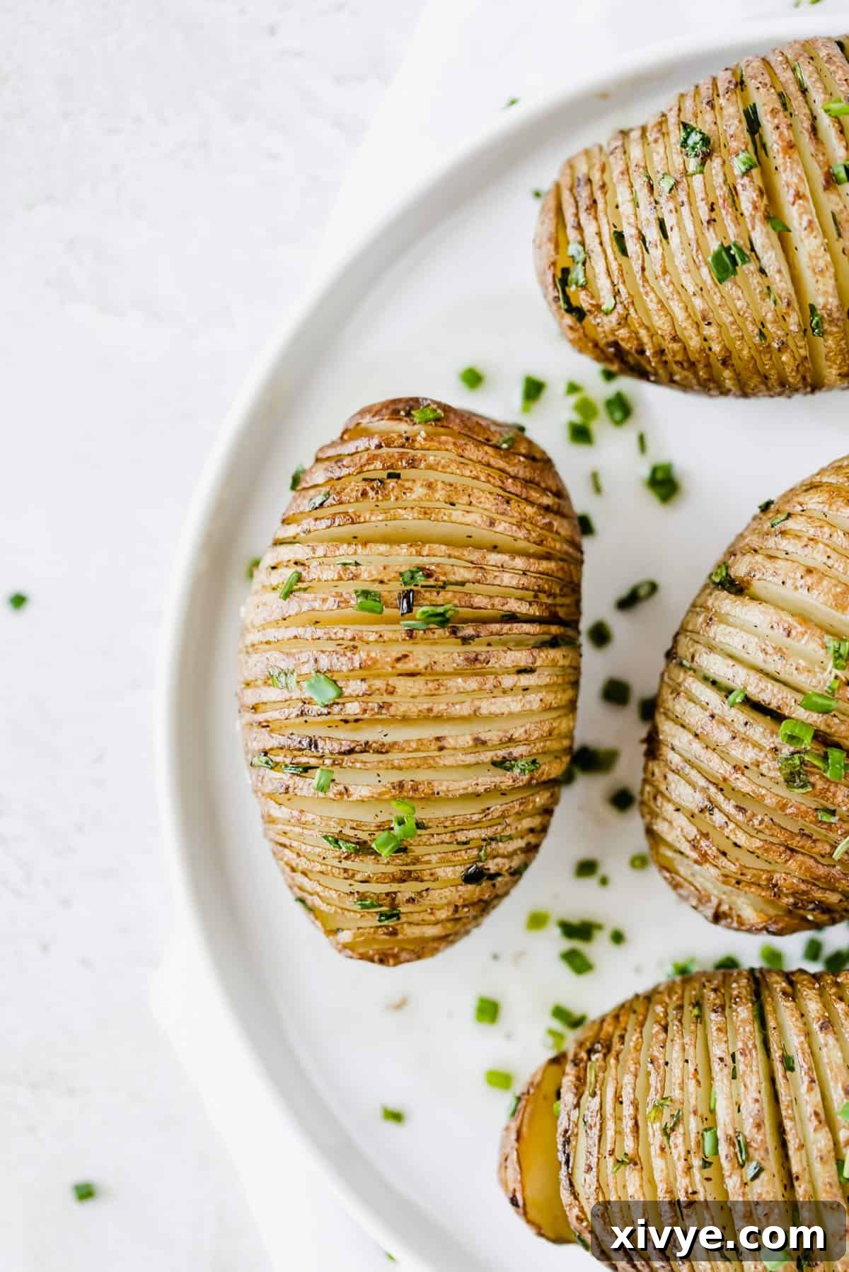 Crispy Air Fryer Hasselback Potatoes: a fun, buttery, and tender side dish. Hasselback Potatoes topped with fresh chives on a white plate.