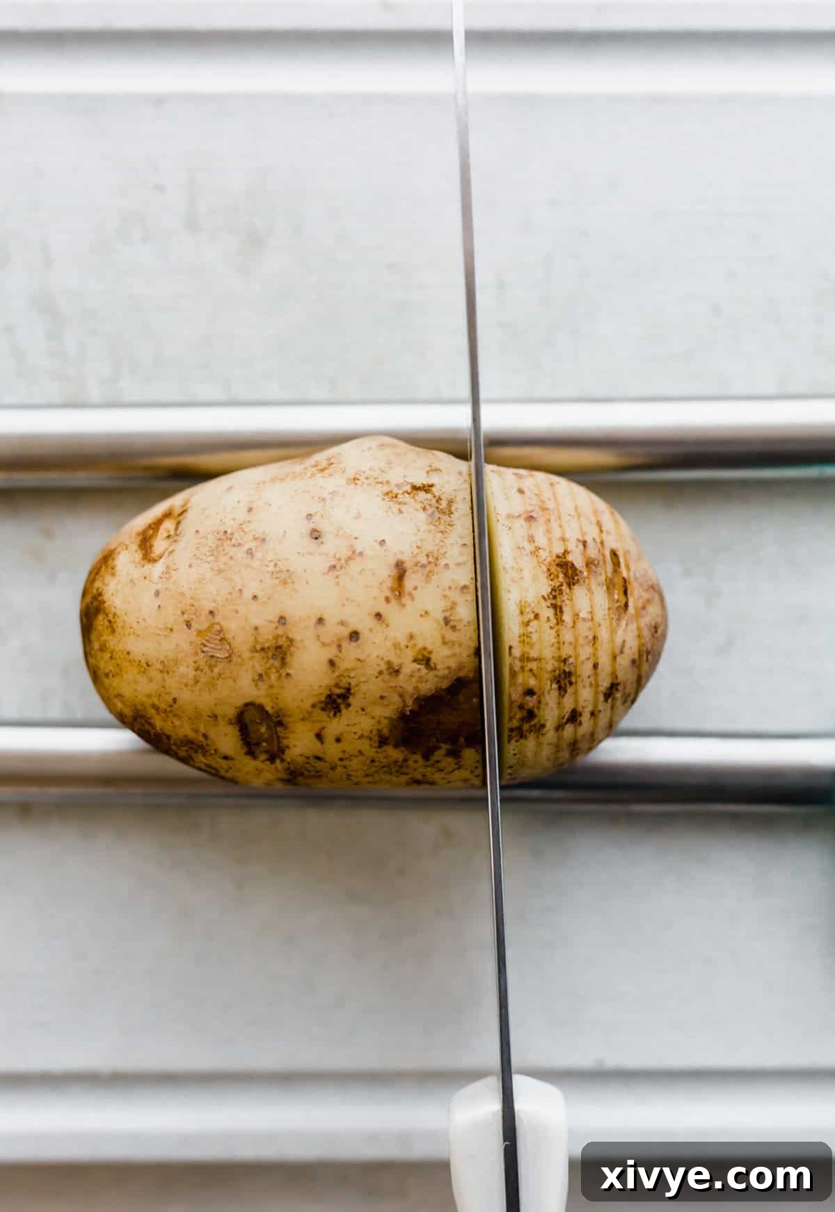 Precisely slicing potatoes for the perfect hasselback effect. A russet potato with a cutting knife cutting through the potato.