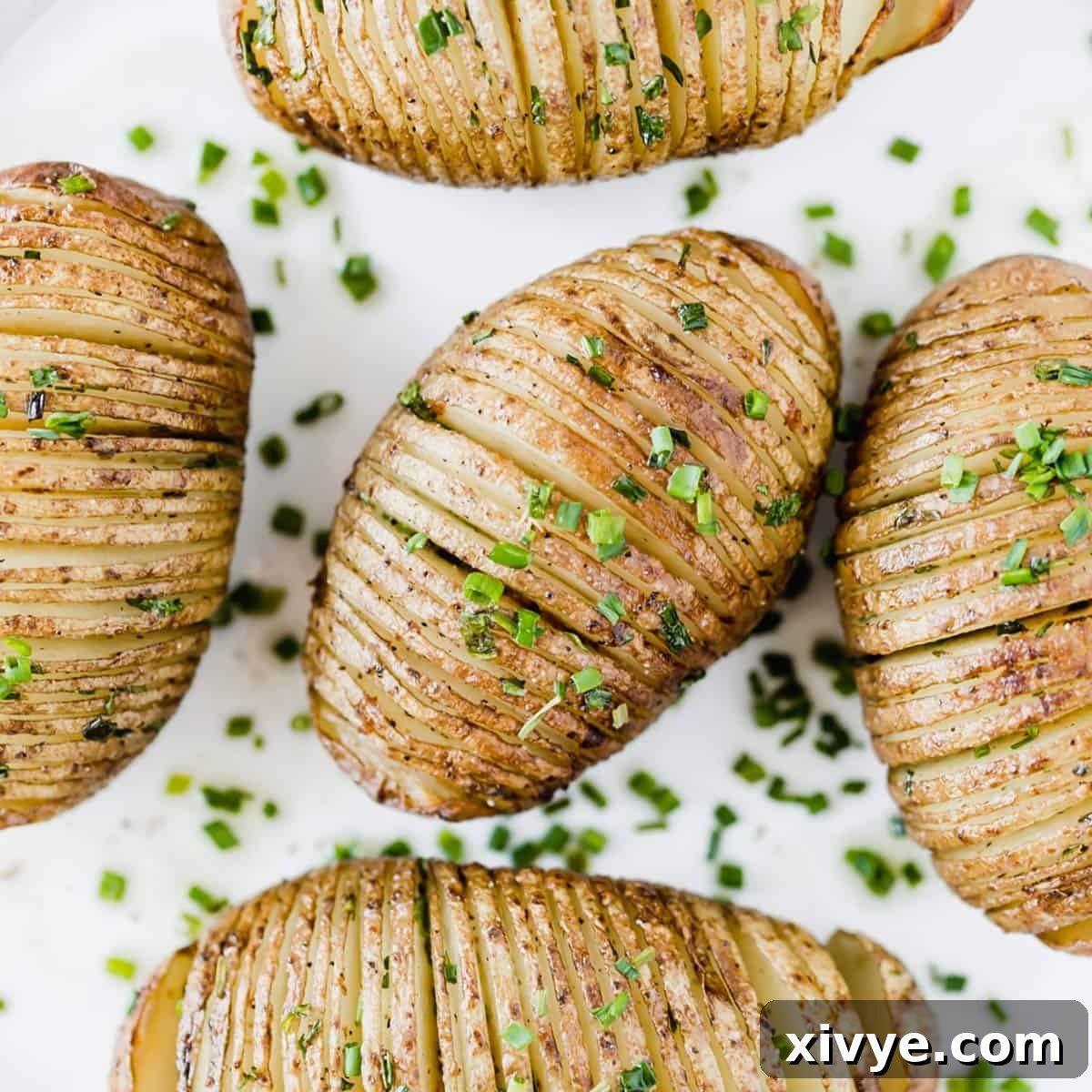 Crispy Air-Fried Hasselback Potatoes 5 Easy Hasselback Potatoes topped with fresh chives on a white background.