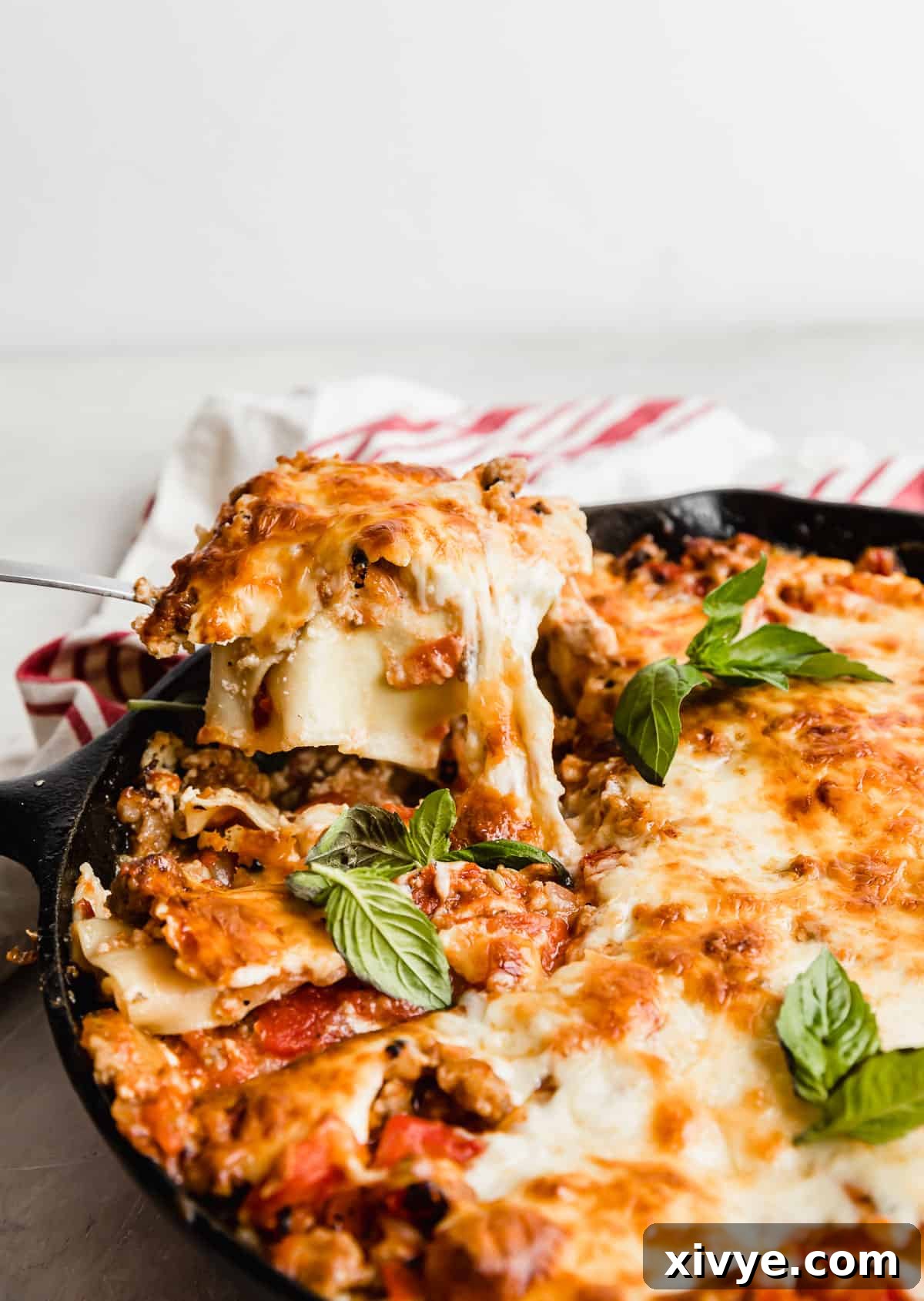 A spoon scooping out Cast Iron Lasagna noodles from a black skillet, revealing cheesy layers.