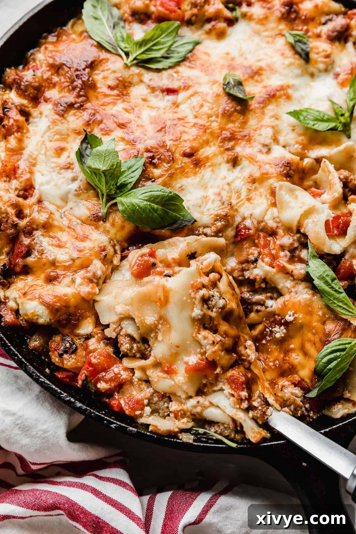 A spoon scooping out Cast Iron Lasagna from a skillet, showing the melted cheese and rich sauce.