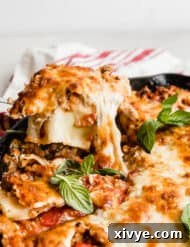 A spoon scooping out Cast Iron lasagna that has been topped with fresh basil.