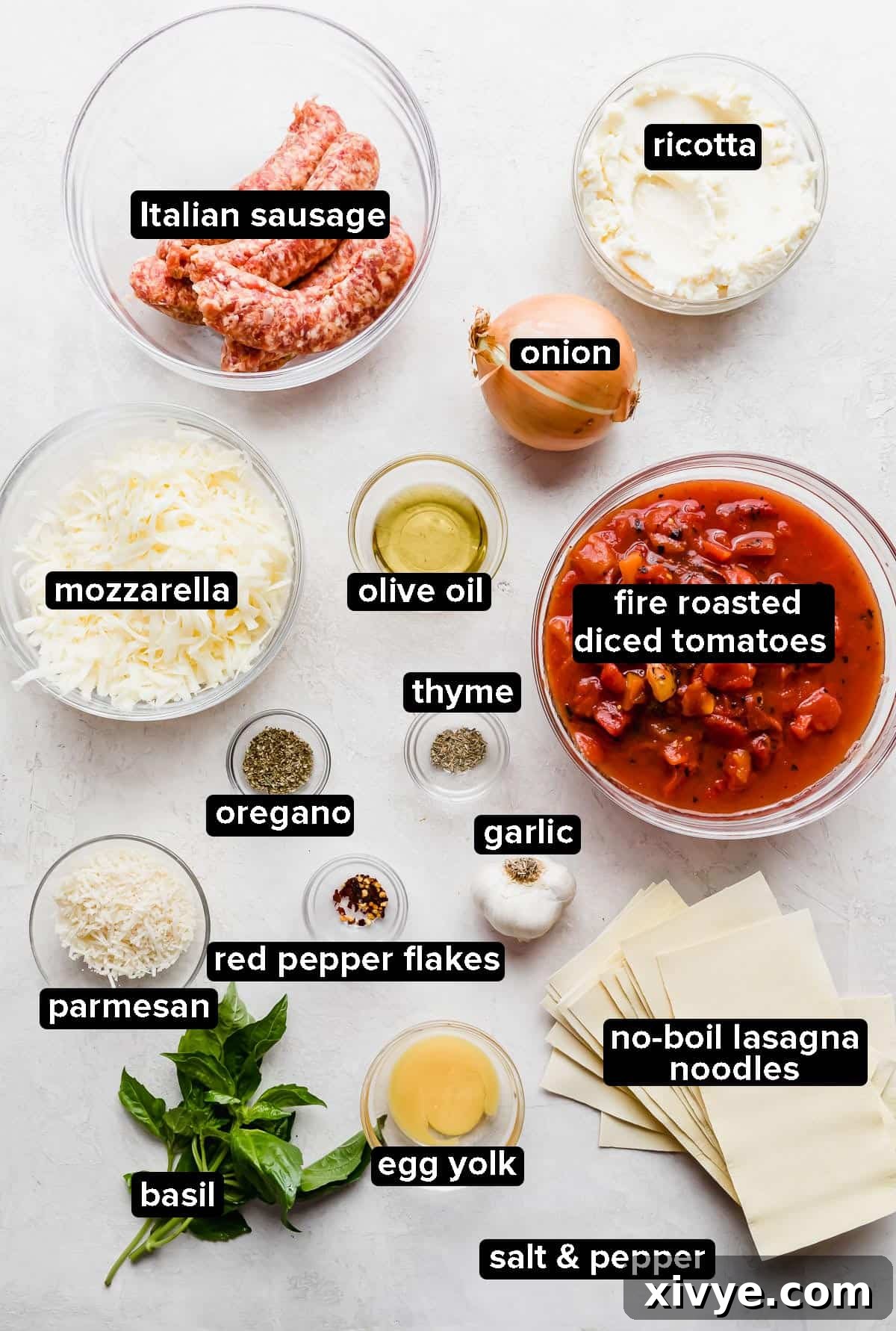 Cast Iron Skillet Lasagna ingredients laid out on a gray background, including tomatoes, ricotta, sausage, and noodles.