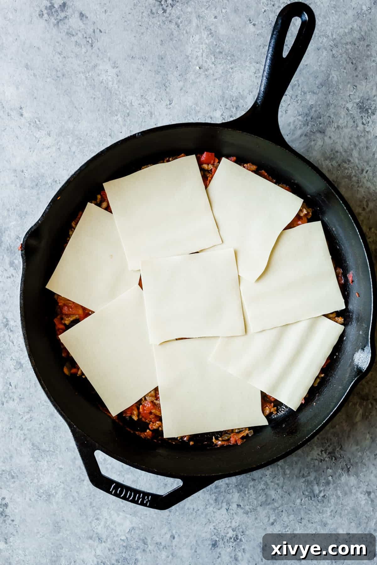 Eight squares of no-boil noodles spread along the bottom of a black skillet, forming the first pasta layer.