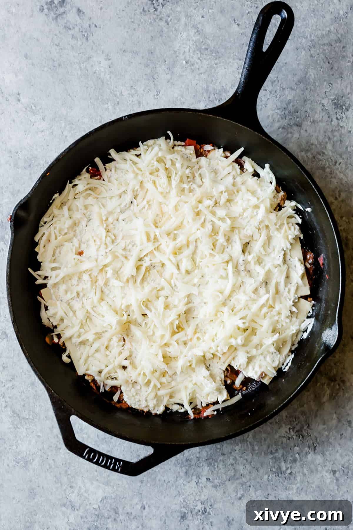 Shredded mozzarella cheese spread overtop of a Cast Iron Lasagna layer, ready for the next step.