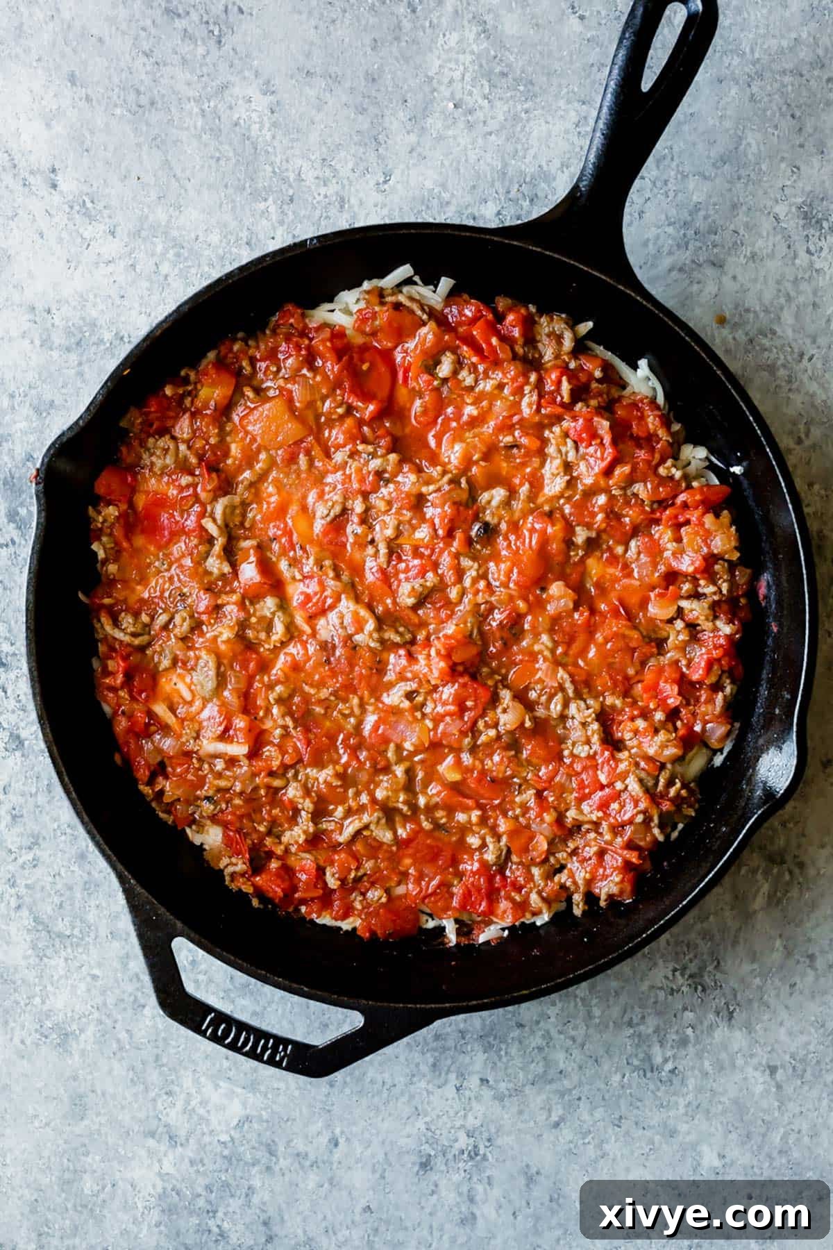 A cast iron skillet with a layered Cast Iron Lasagna mixture in it, showing the progress of assembly.