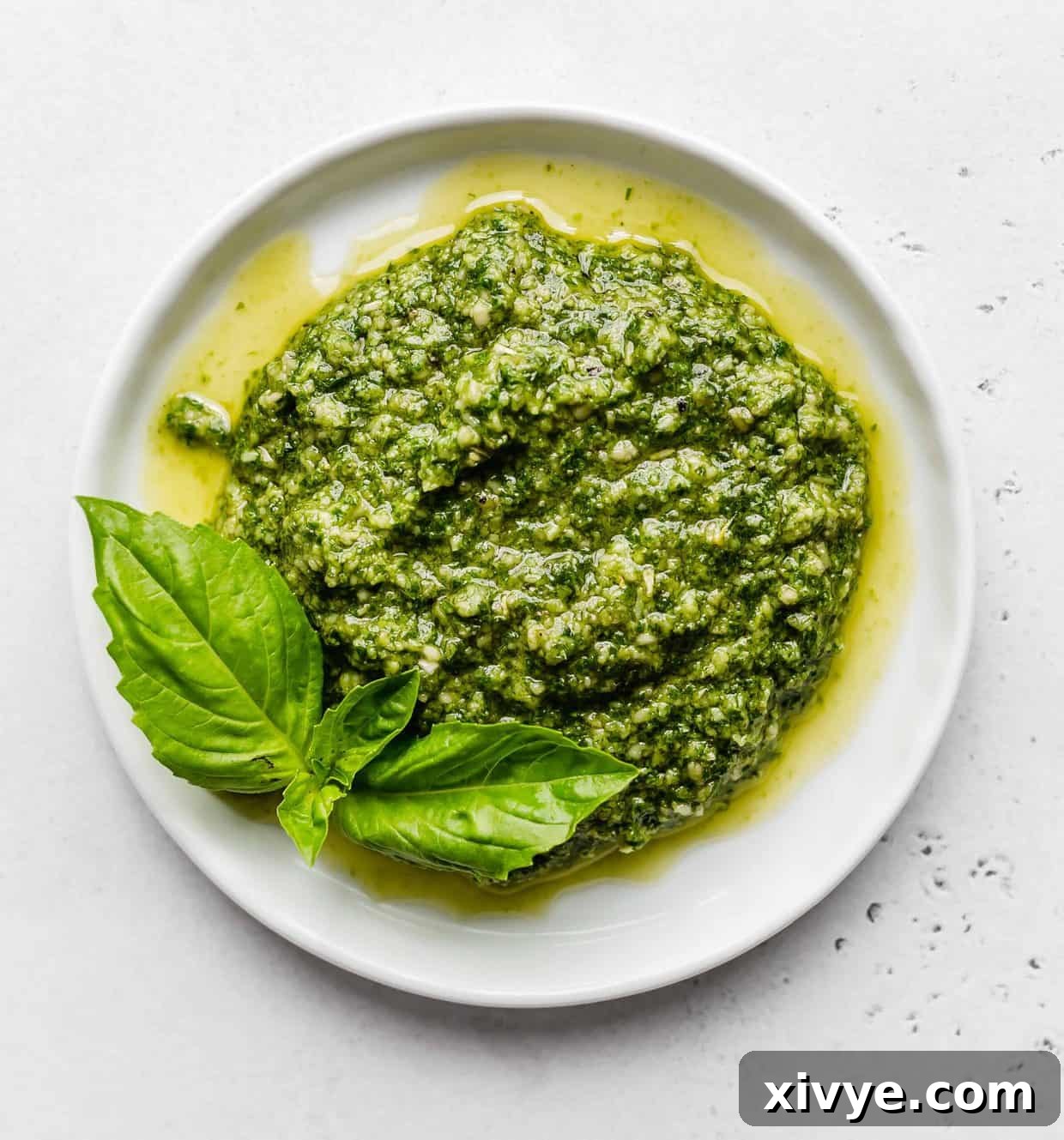 A white plate with fresh basil pesto on it, garnished with basil leaves.