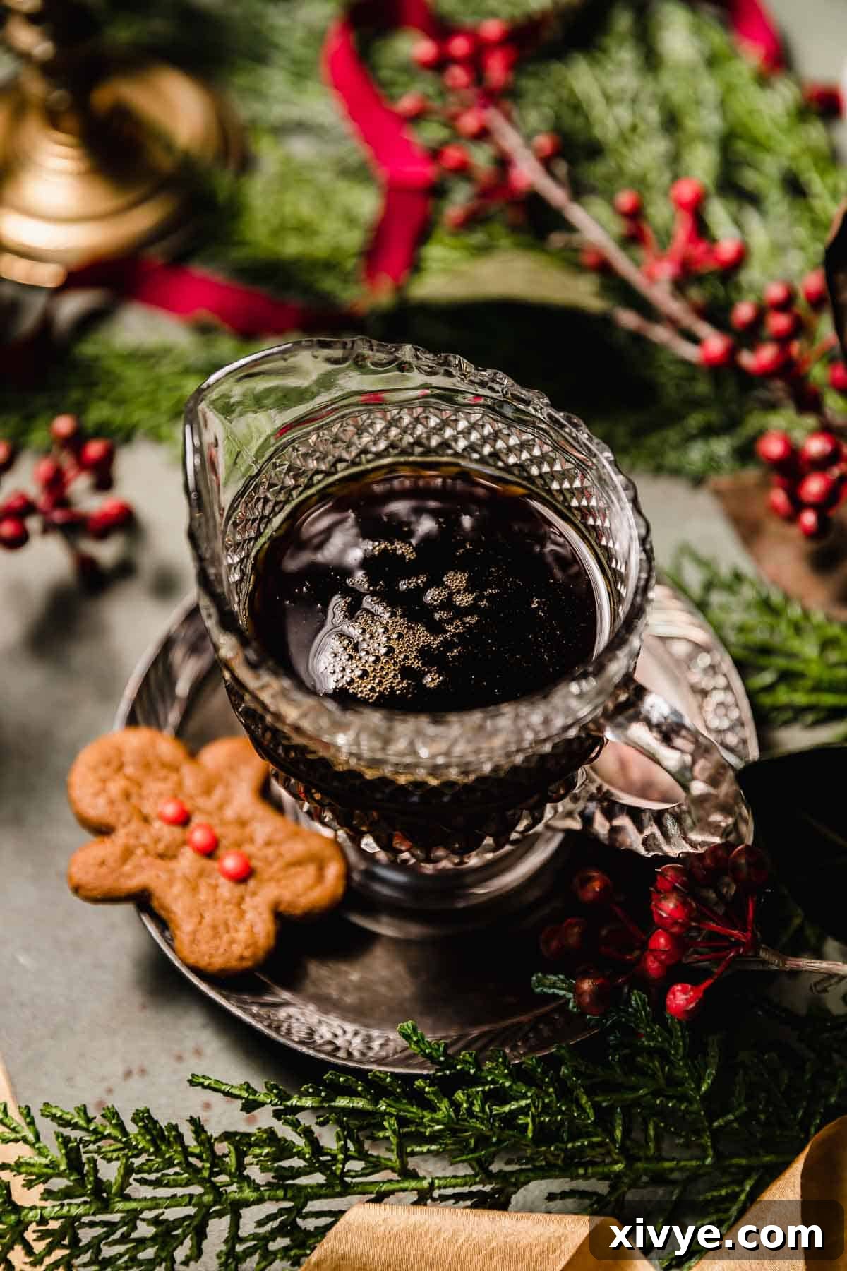 Gingerbread Syrup in a clear glass pouring cup with a small gingerbread man cookie to the left of the syrup bottle.