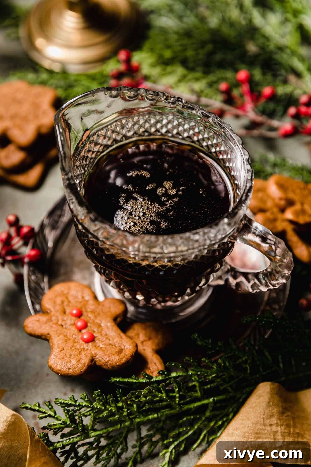 Gingerbread Syrup in a clear cup surrounded by baked gingerbread cookies, Christmas greenery, and red berries.