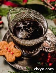 Gingerbread Syrup surrounded by red berries, Christmas greenery, and baked gingerbread cookies with red candy buttons on them.