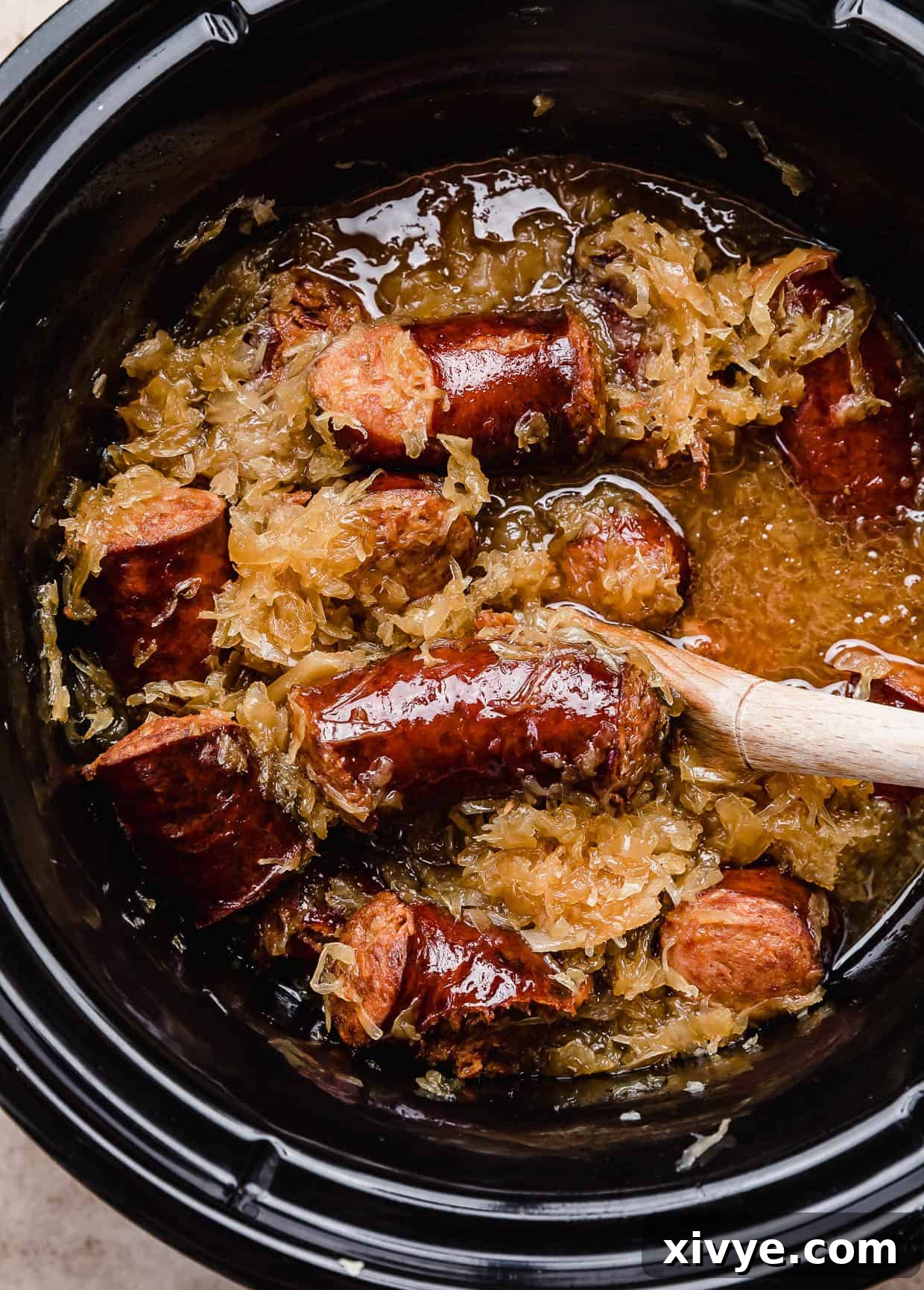 A black crock pot filled with cooked kielbasa and sauerkraut, ready to serve.
