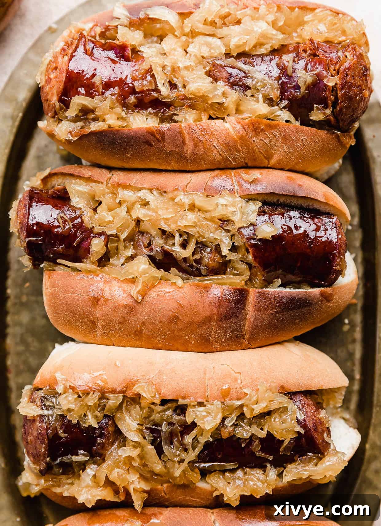 Three hoagie buns filled with Crock Pot Kielbasa and Sauerkraut on a brass serving plate, garnished with fresh parsley.