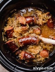 A black crock pot filled with cooked kielbasa and sauerkraut.