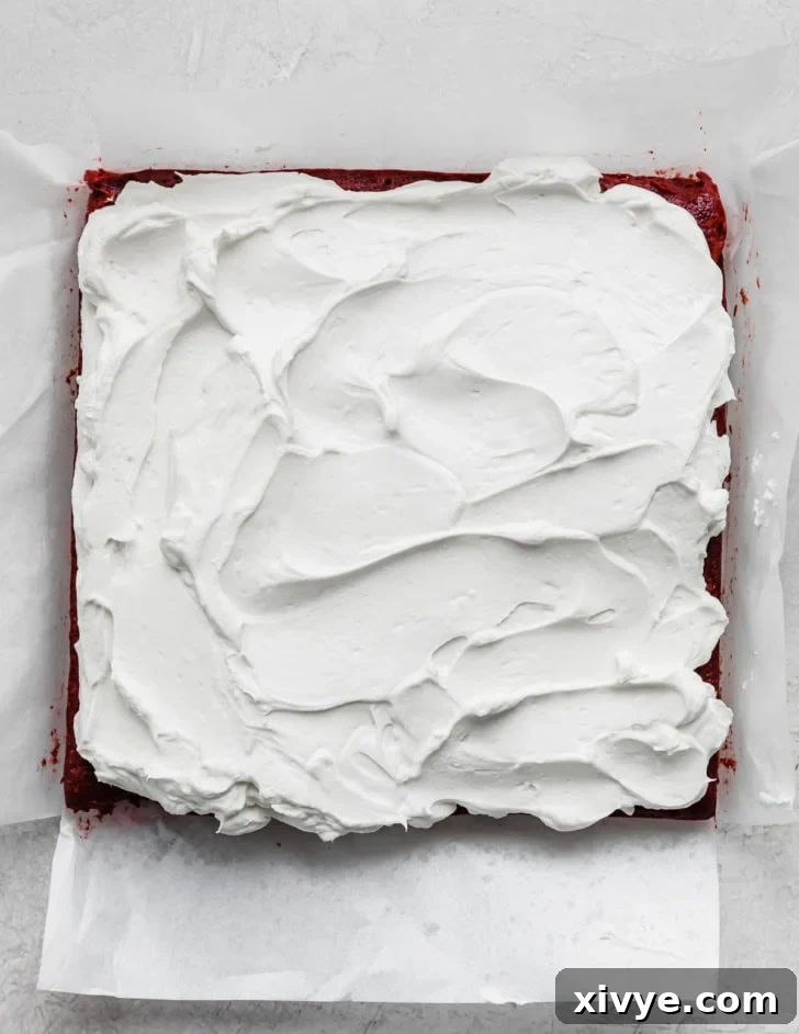 Baked red velvet brownies topped with a white whipped cream cheese frosting.