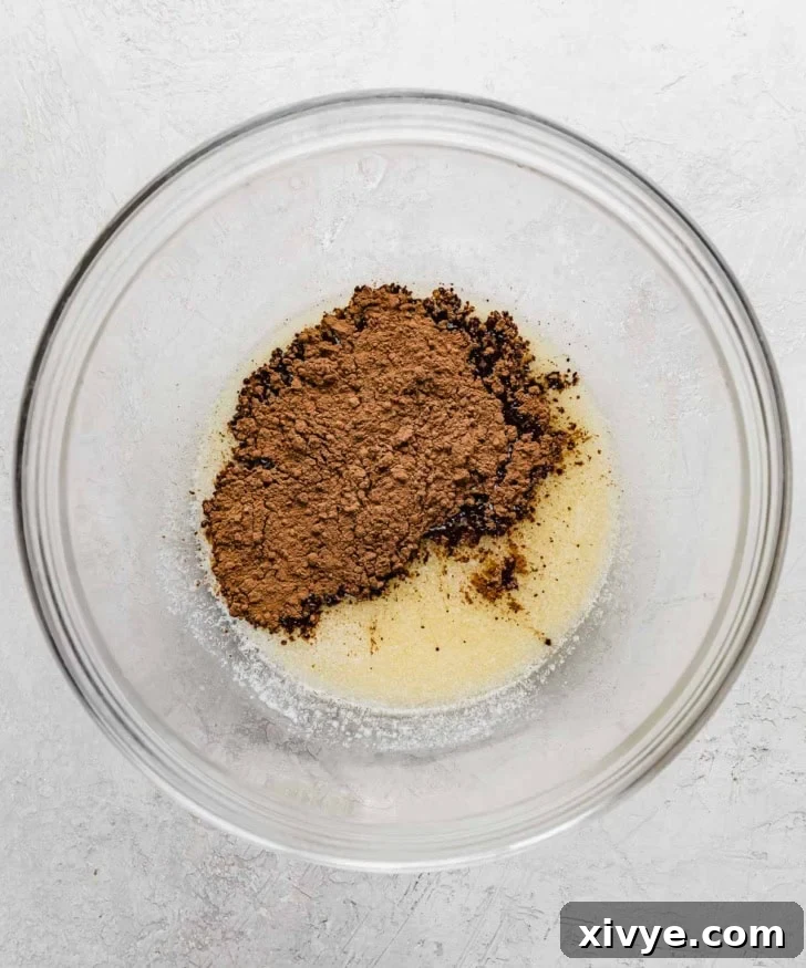 Melted butter and cocoa powder in a glass bowl on a gray surface.