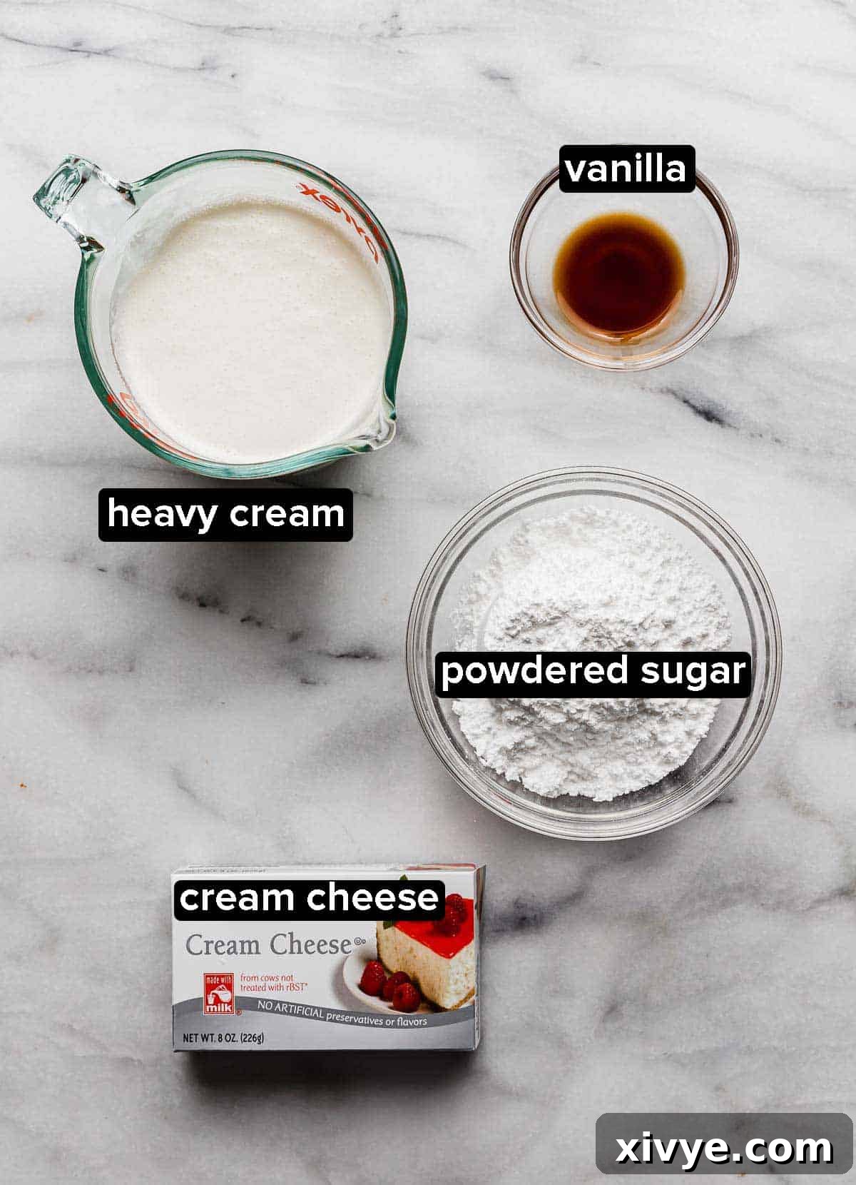 Cream Cheese Whipped Cream Frosting ingredients on a white marble table, heavy cream, vanilla, cream cheese, and powdered sugar.