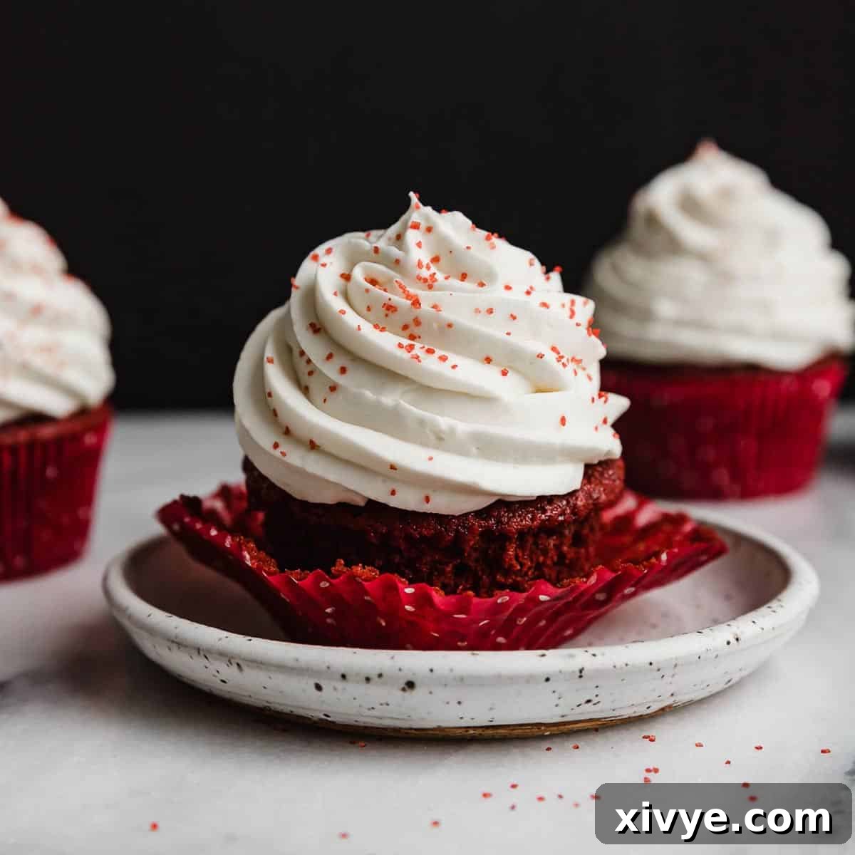 A red velvet cupcake topped with Cream Cheese Whipped Cream Frosting with red sugar sprinkles.
