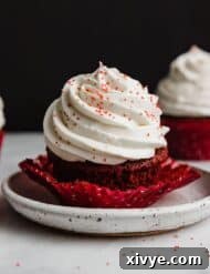 A red velvet cupcake topped with Cream Cheese Whipped Cream Frosting with red sugar sprinkles.