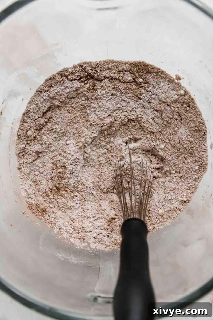 A whisk mixing dry ingredients used in a red velvet cupcake recipe.