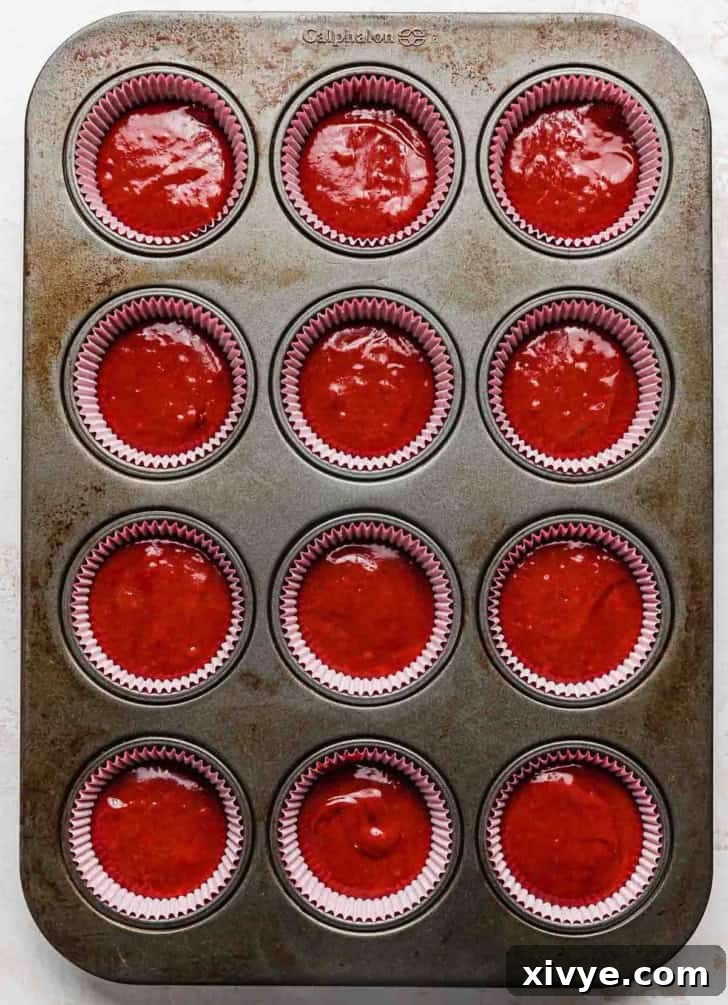 Twelve capacity cupcake pan filled with cupcake liners and vibrant red velvet cupcake batter in each liner.