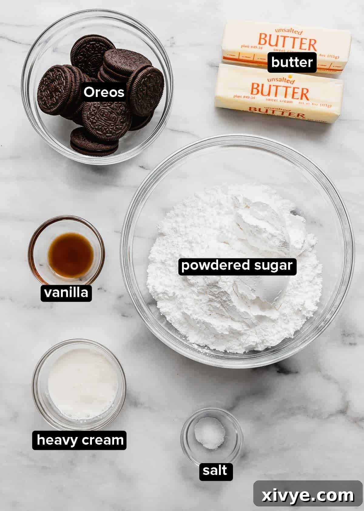 Ingredients for Oreo Frosting laid out on a clean white surface: softened butter, heavy cream, whole Oreo cookies, fine salt, powdered sugar, and pure vanilla extract.