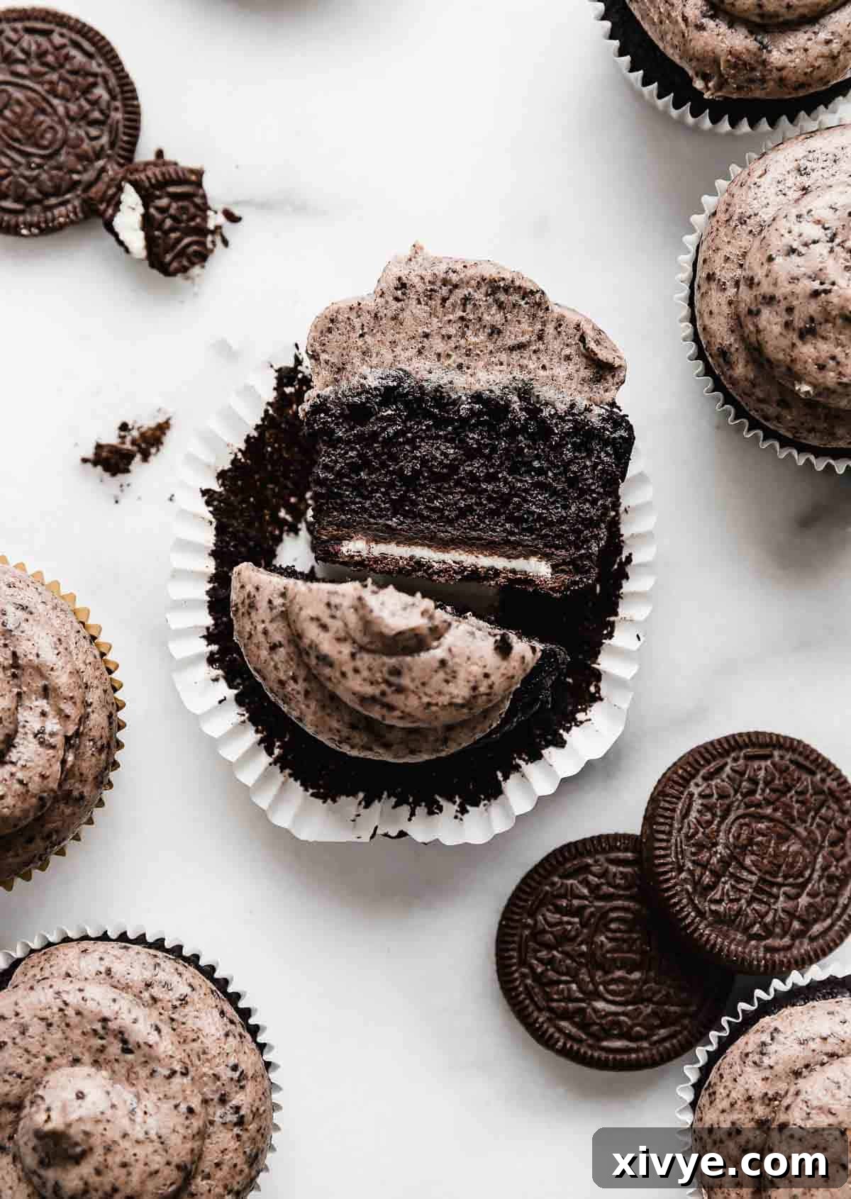 A delicious Oreo Cupcake, elegantly sliced in half to reveal its perfect layers, resting on a sophisticated white marble background.