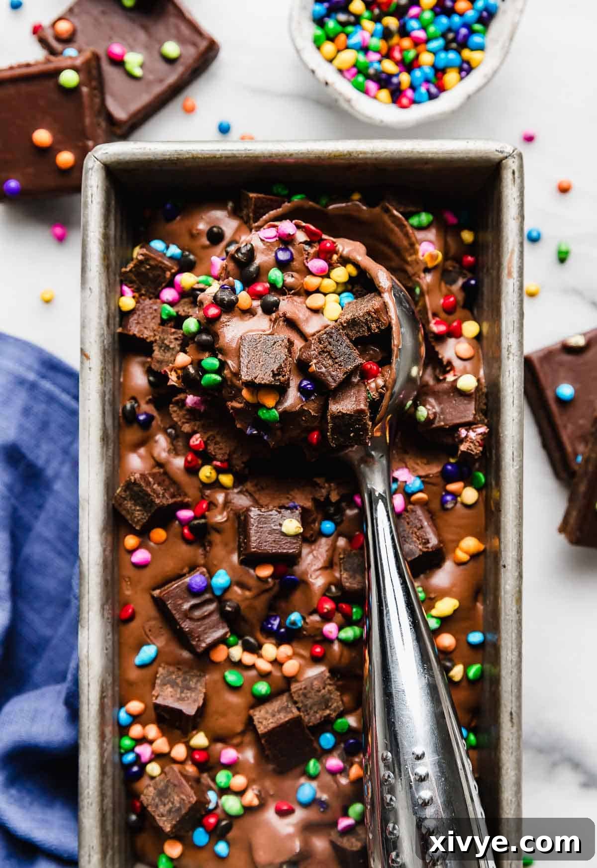 Stardust Brownie Galaxy 2 An ice cream scoop scooping out Cosmic Brownie Ice Cream from a rectangular bread pan on a white marble background.