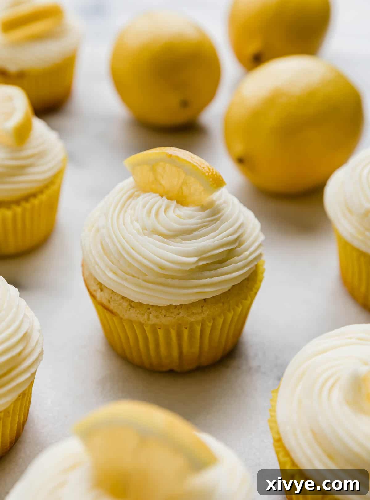 Lemon cupcakes topped with Lemon Buttercream and a fresh lemon wedge on a white background.