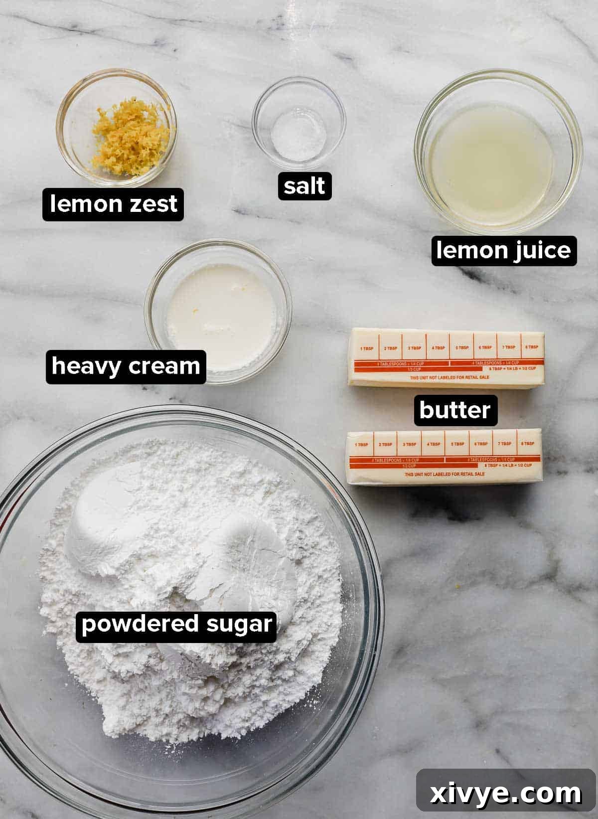 Lemon Buttercream frosting ingredients portioned into glass bowls on a white marble table.