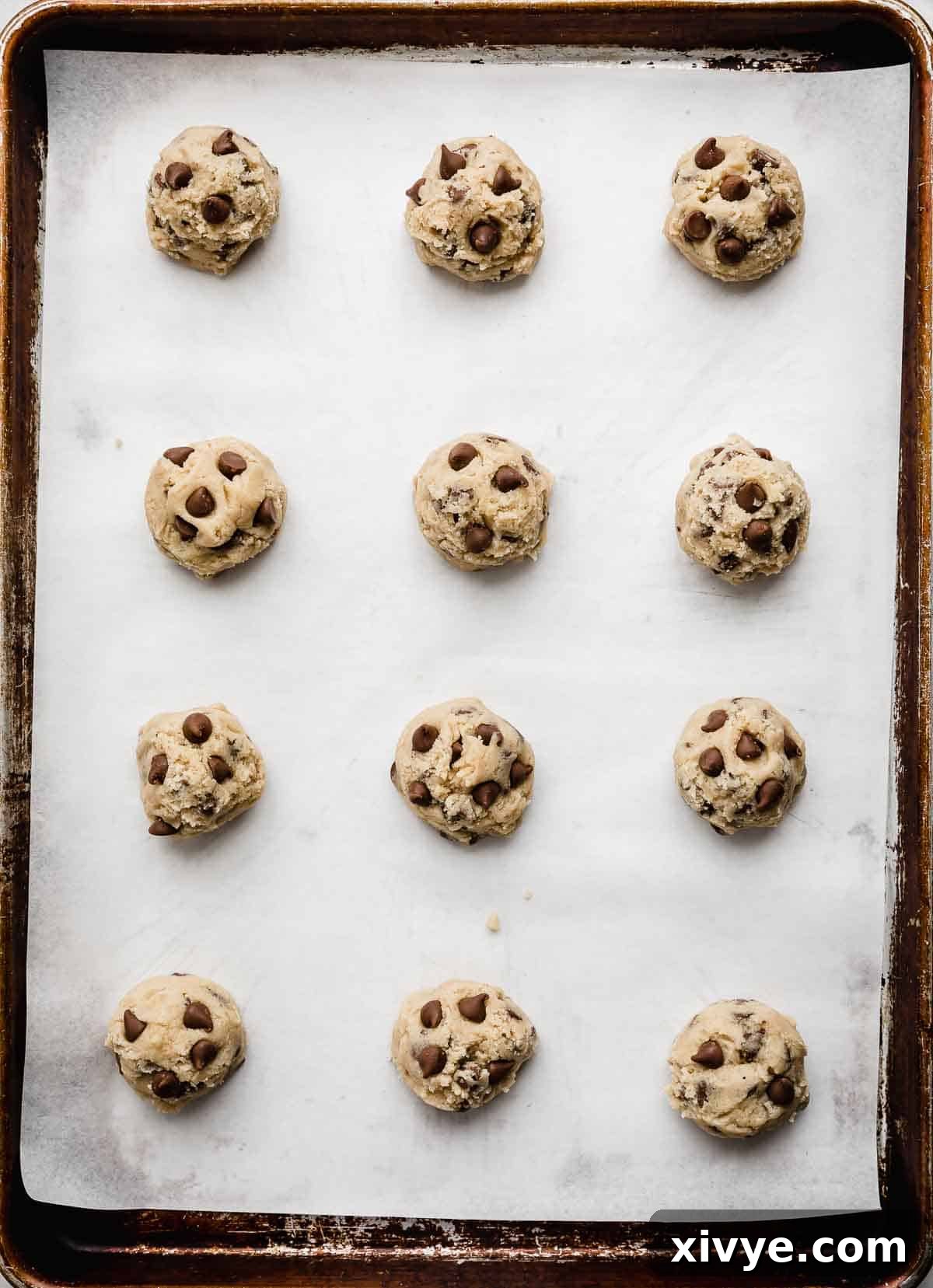 Homemade Milk Chocolate Chip Perfection 5 Perfectly portioned Milk Chocolate Chip Cookie dough balls arranged neatly on a white parchment-lined baking sheet, spaced adequately for baking.