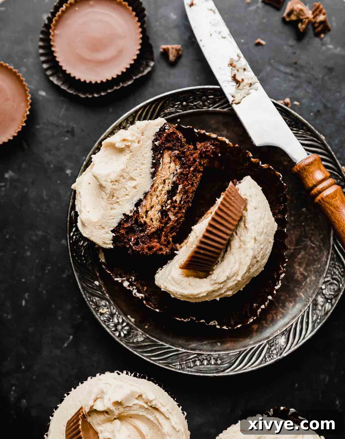 A Reeses Cupcake on a plate that's cut in half showing the inside of a Reeses peanut butter cup exposed in the middle of the cupcake.