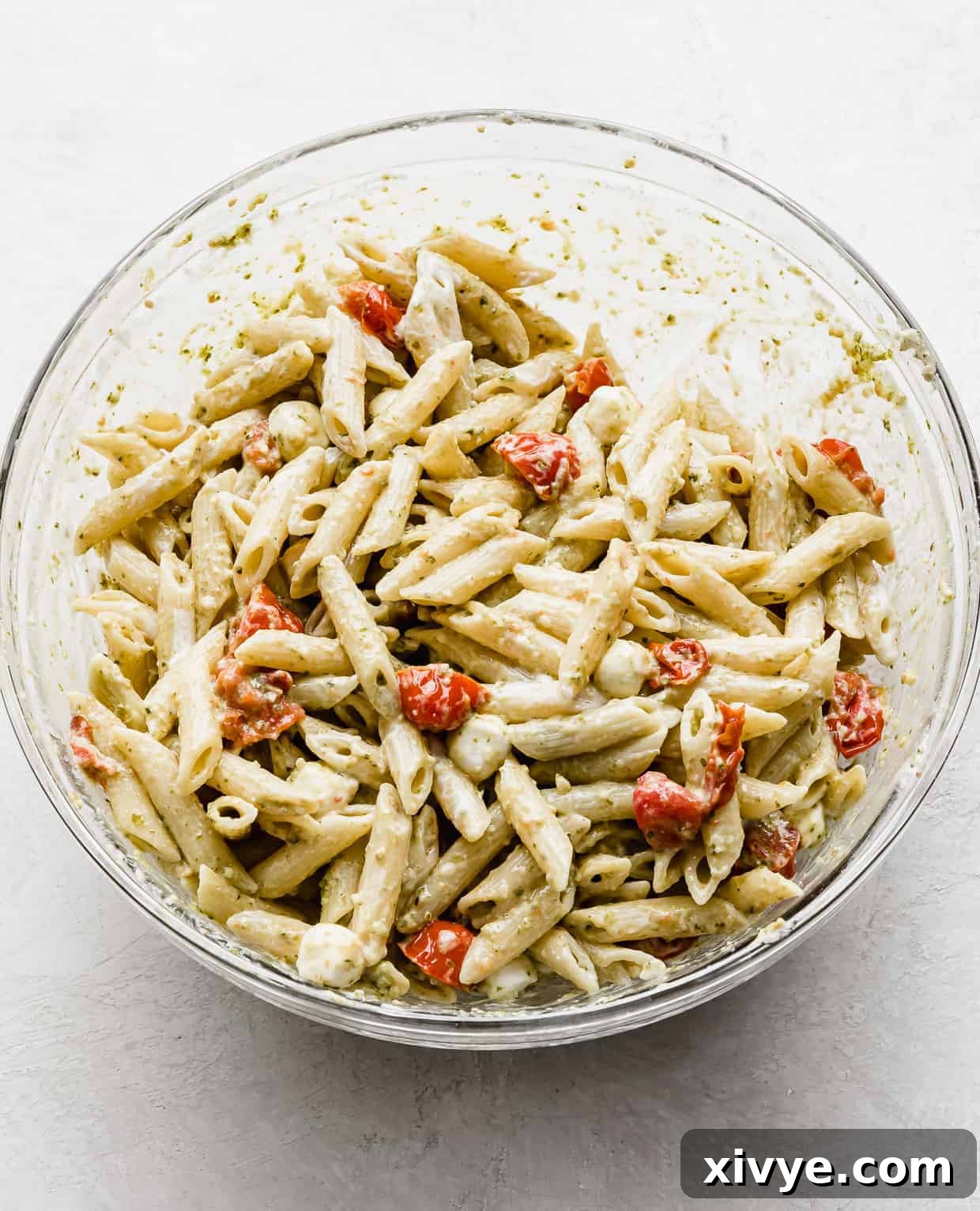 A glass bowl with creamy pesto pasta with tomatoes and mozzarella. 