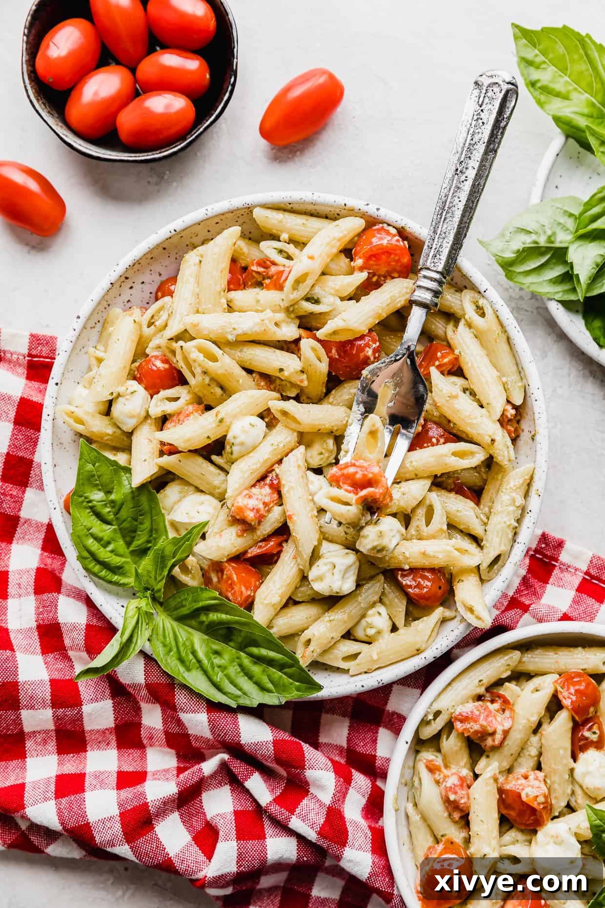 A white plate with Pesto Pasta with Tomatoes and mozzarella balls.