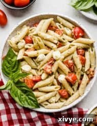 A bowl of creamy pesto pasta with tomatoes and mozzarella balls.