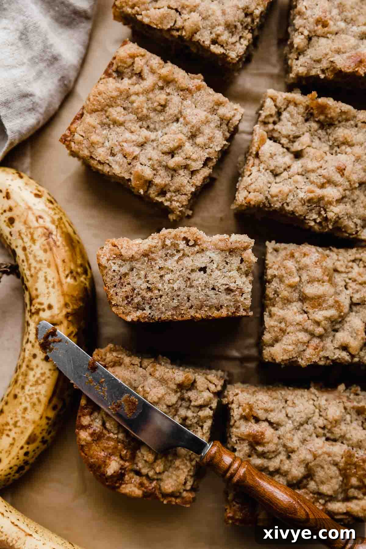 Banana Coffee Cake with streusel topping cut into squares on a Kraft parchment paper.