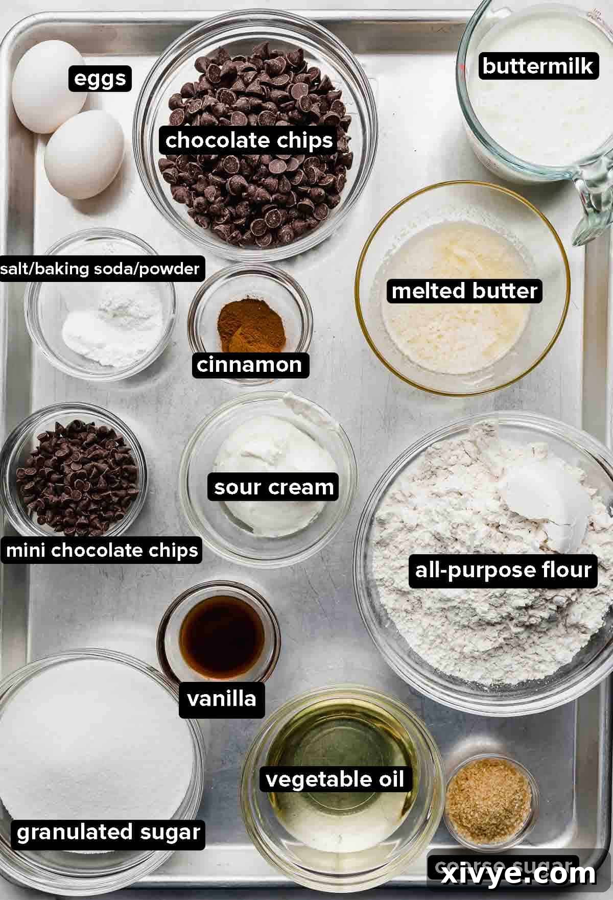 Bakery Style Chocolate Chip Muffins ingredients portioned into glass bowls on a silver baking sheet, ready for mixing.