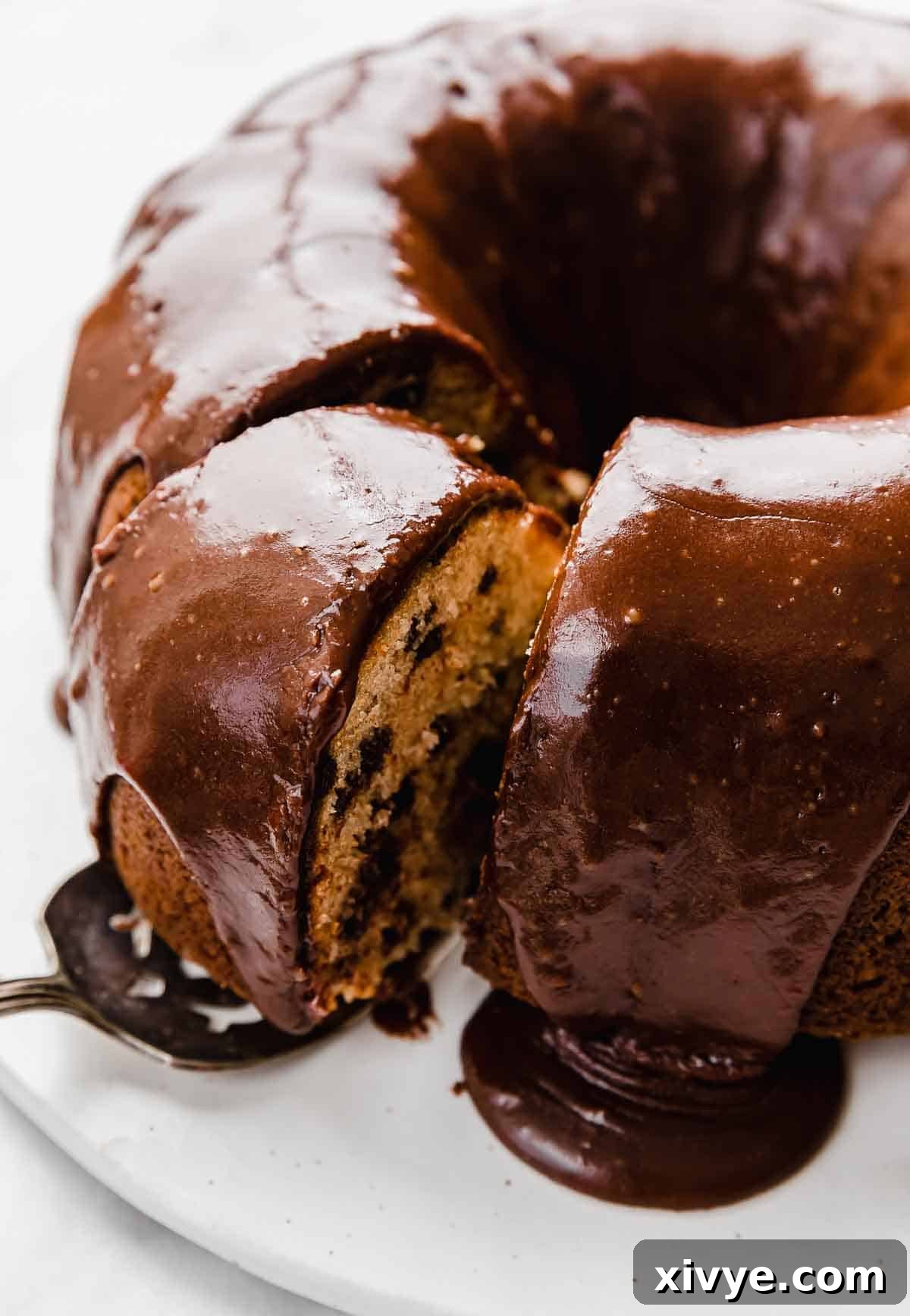 Decadent Chocolate Chip Crown Cake 3 Chocolate frosting covered Chocolate Chip Bundt Cake on a white plate with a slice being removed from the cake.