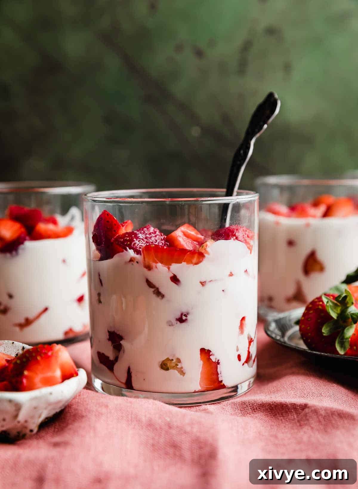 Creamy Strawberry Indulgence 6 Three clear cups filled with Strawberries and Cream (Fresas con Crema) on a red linen cloth against a textured brown and green background.