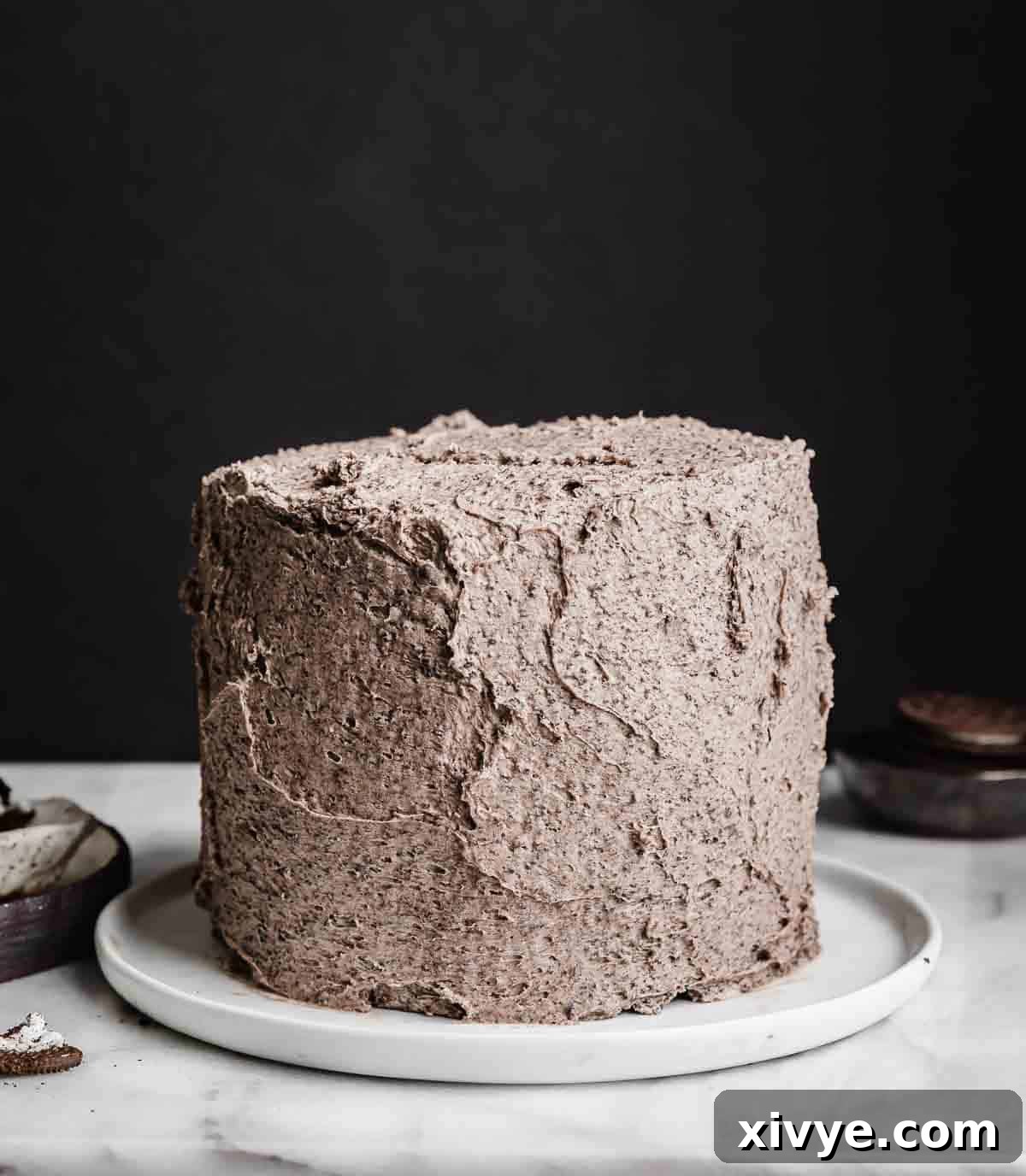 A fully frosted Oreo cake, generously covered in creamy Oreo frosting, presented against a dark, elegant background.