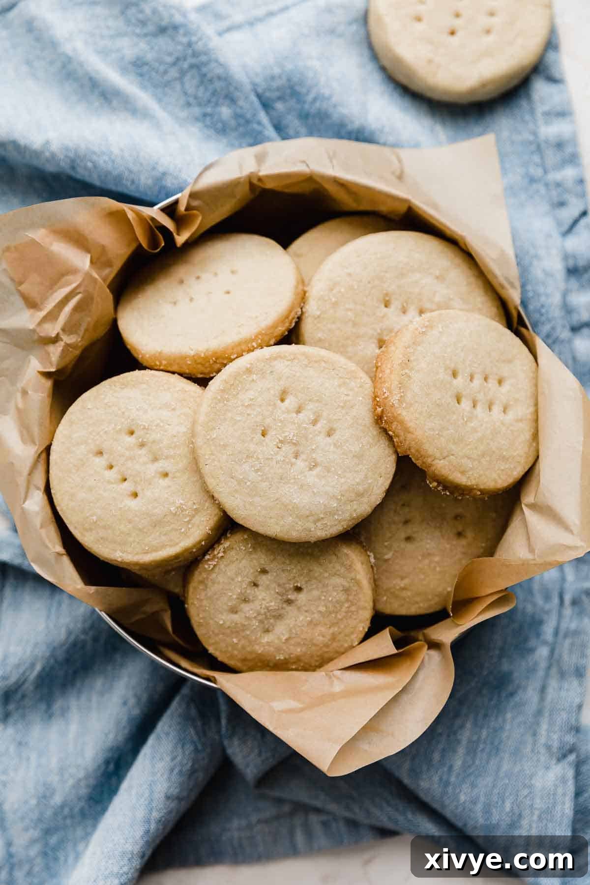 An inviting overhead shot of Grandma's Shortbread Cookies, perfectly round and arranged in a decorative tin, resting on a soft light blue napkin.