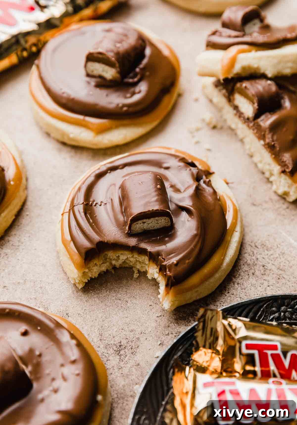 A Twix Cookies made with a shortbread cookie base, topped with caramel, chocolate and a Twix bar on a light brown background.