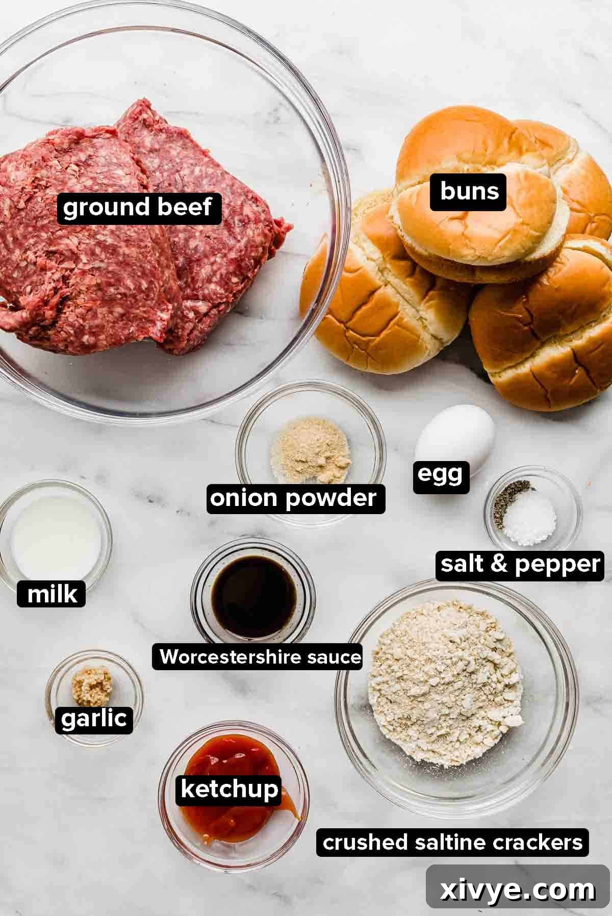 Signature Steakhouse Burgers 3 Steakhouse Burgers ingredients on a white marble background: ground beef, buns, ketchup, onion powder, egg, salt and pepper, garlic, milk, and saltine crackers.