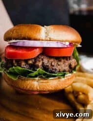 A hamburger bun with tomato, purple onion, and lettuce with a large Steakhouse Burgers patty against a dark brown background.